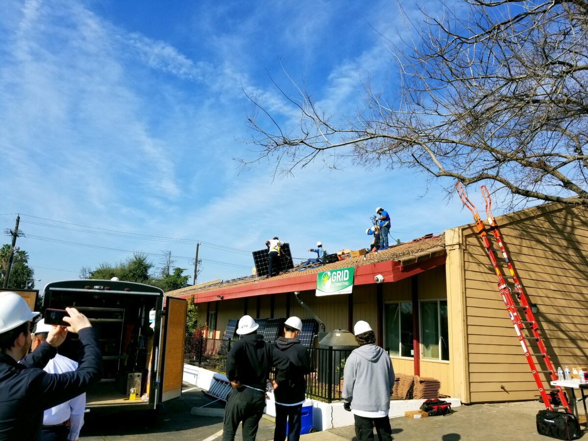 Workers installing solar panels on a residential home's roof with GRID logo visible