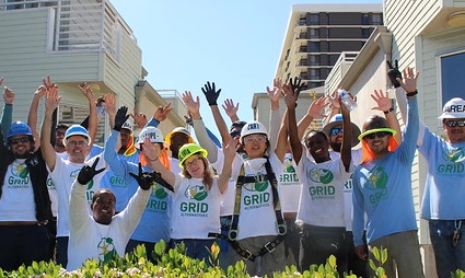 Group of volunteers in GRID shirts with arms raised celebrating at an outdoor community event