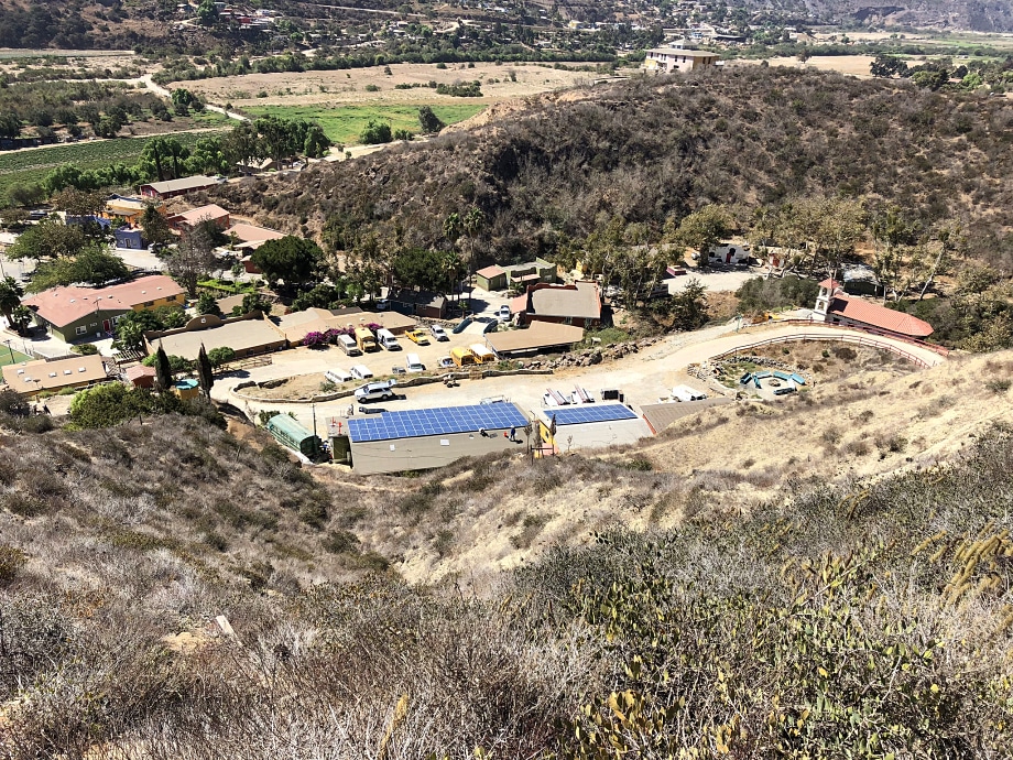 Aerial view of hillside property with solar panels, buildings, and surrounding farmland and trees