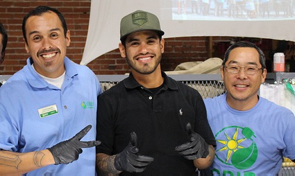 Three men posing together indoors, wearing casual clothing and smiling at the camera during what appears to be a community event