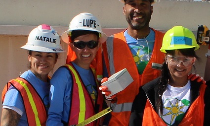 Four construction workers in hard hats and safety vests smiling at camera