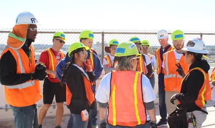 Group of construction workers in safety vests and hard hats gathered at a job site meeting