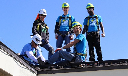 Construction workers in safety gear on a roof against blue sky