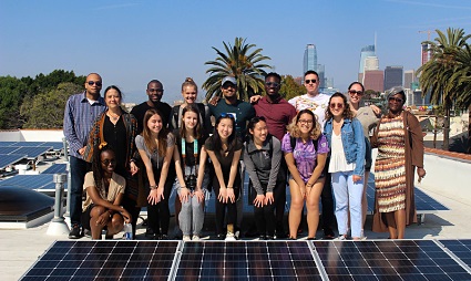 Group of people posing with solar panels on a rooftop with city skyline in background