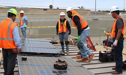 Construction workers installing solar panels on a flat rooftop with safety equipment
