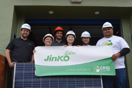 Team holding Jinko Solar banner with solar panel installation