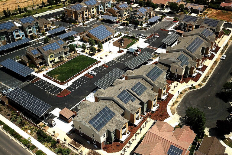 Aerial view of residential neighborhood with solar panels on rooftops and a parking lot with green space