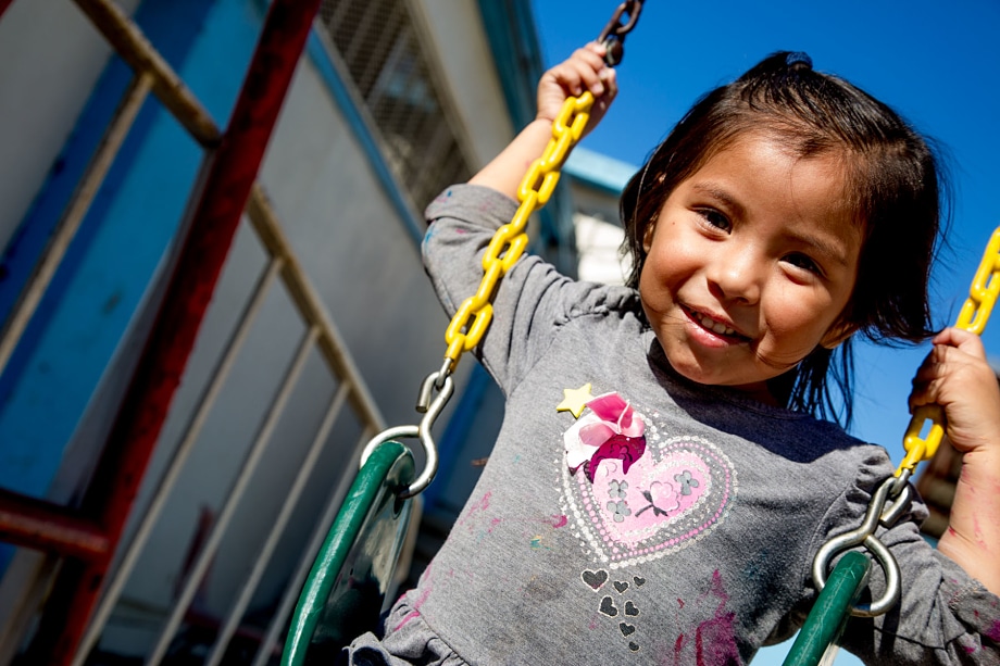Young child smiling on a playground swing with yellow chain against blue sky