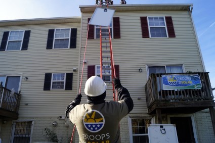 A KPMG Veteran volunteer guides a solar panel to the roof