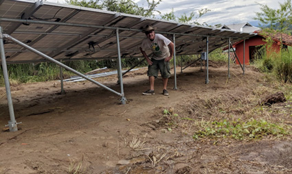 Person working under solar panel structure at rural farm site