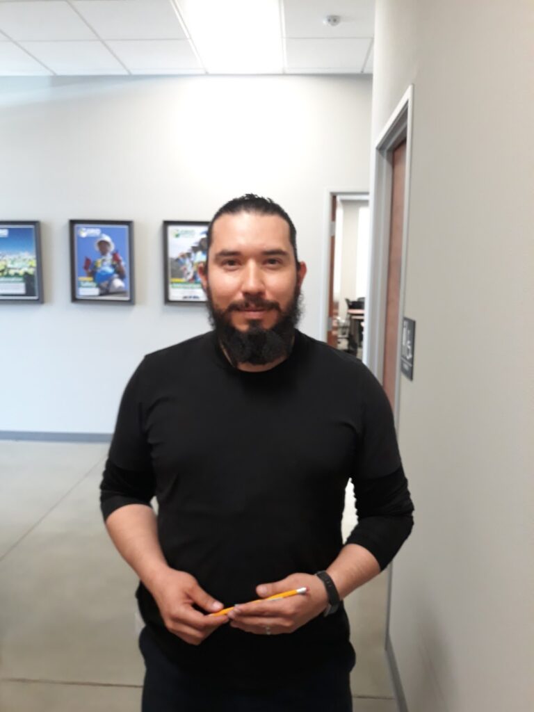 Man with beard in black long-sleeved shirt holding pencil in office hallway