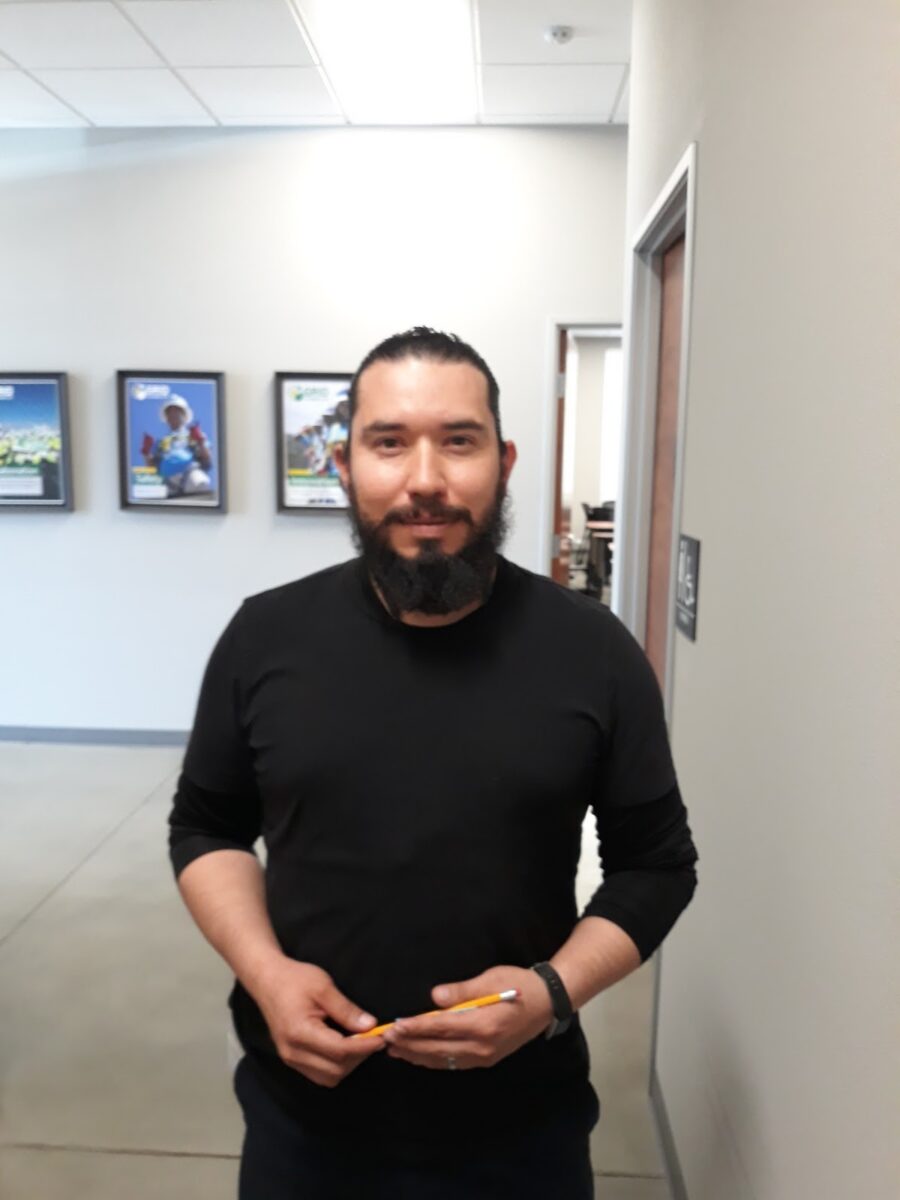 Man with beard in black long-sleeved shirt holding pencil in office hallway