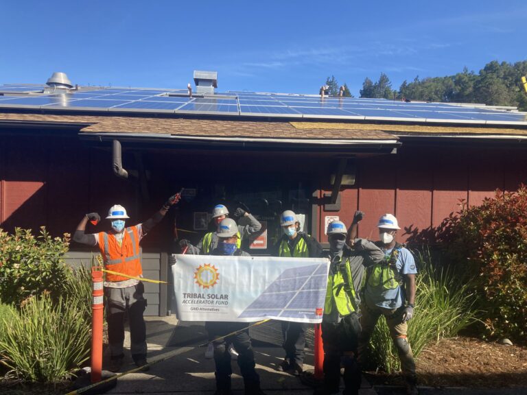 Tribal Solar Accelerator Fund team celebrates solar installation on building roof with blue panels