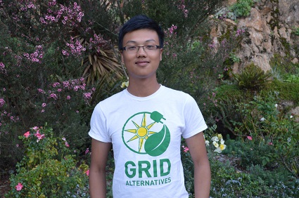 Person wearing GRID Alternatives t-shirt smiling in front of flowering vines