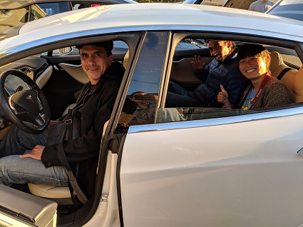 Man smiling in driver's seat of white electric vehicle with passengers visible in back seat