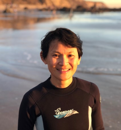 Young person in wetsuit at beach at sunset, smiling at camera