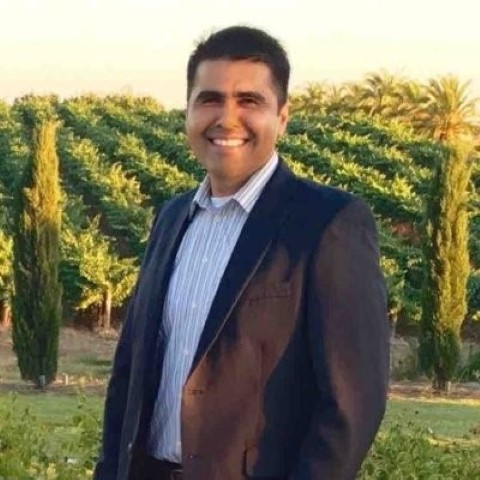 Man in brown blazer and blue shirt smiling in vineyard setting