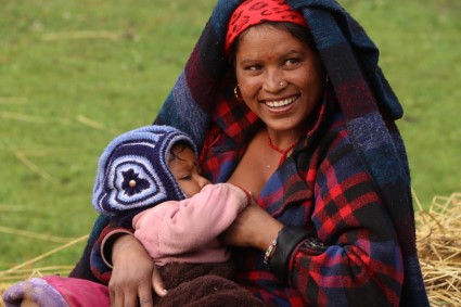 Smiling young woman in colorful blankets holding a newborn baby outdoors