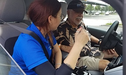 Woman in blue shirt and man in camouflage discussing vehicle controls inside a car