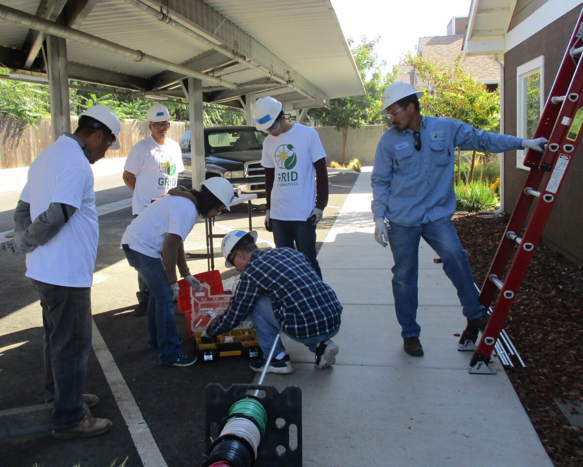 Group of volunteers in GRID t-shirts and hard hats installing solar panel equipment during a community service project