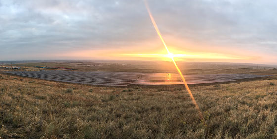 Sunset over sprawling grassland with solar panel array in distance