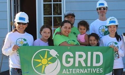 Group of volunteers in hard hats holding GRID Alternatives banner at community event