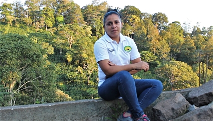 Woman in white shirt sitting on concrete ledge with forest background
