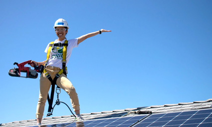 Construction worker in safety gear standing on solar panels, pointing outward against blue sky