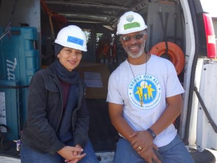 Two people in hard hats smile at camera inside a work van labeled "Clovis