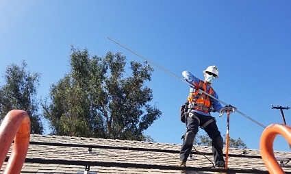 Worker in safety gear installing roofing materials on residential structure under clear sky