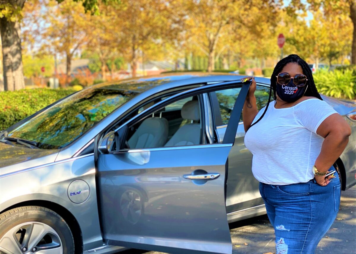 Woman wearing Census 2020 mask standing by blue car in park