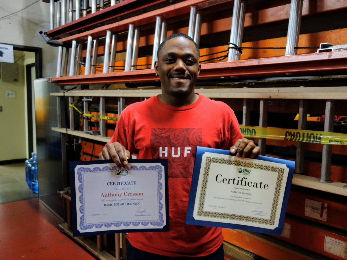 Man holding two certificates for Basic Solar Training and Anthony Crosson in warehouse with shelving