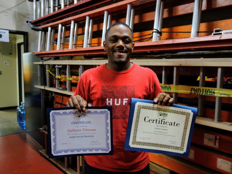 Man holding two certificates for Basic Solar Training and Anthony Crosson in warehouse with shelving
