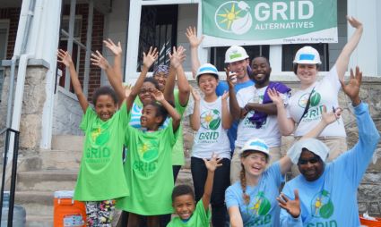 Group of volunteers in green and blue shirts celebrating under Grid Alternatives sign