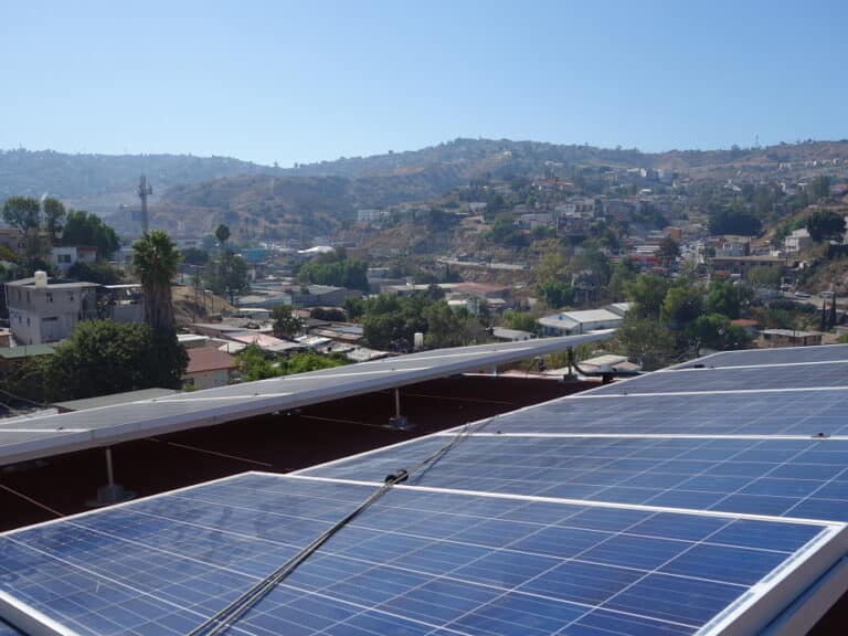Solar panels on rooftop overlooking hillside neighborhood with buildings and green vegetation