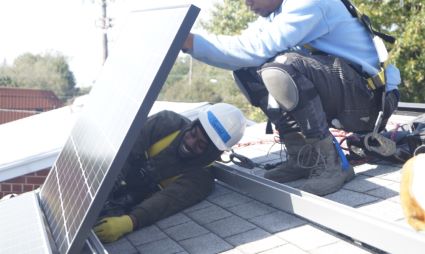 Worker installing solar panels on residential roof in sunlight