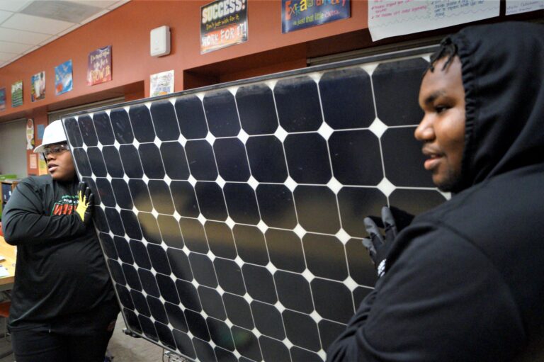 Students examining a large solar panel in a classroom with orange walls and educational posters