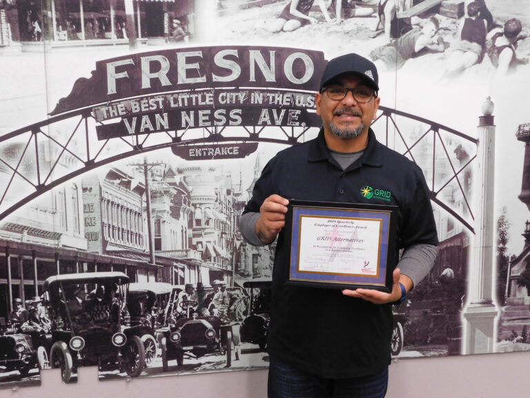 Man holding award certificate in front of Fresno Van Ness Ave vintage mural