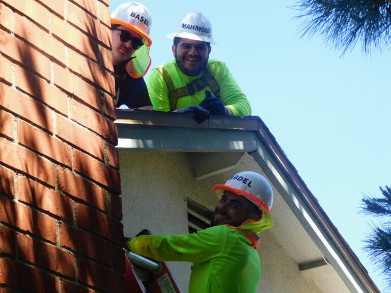 Three construction workers in high-visibility gear and hard hats on a building exterior during work