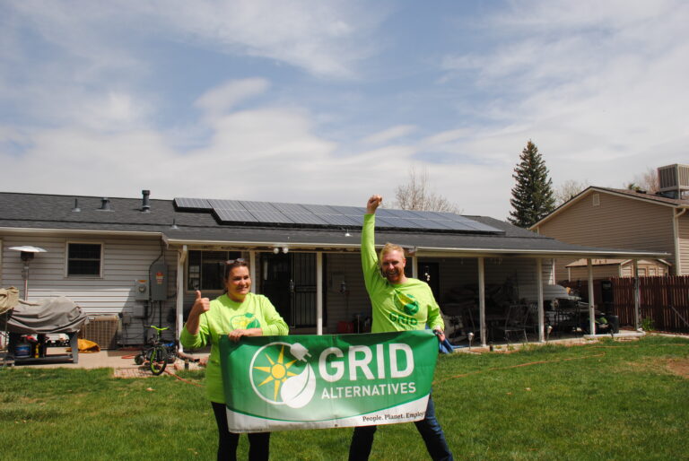 Two people hold up a GRID banner in front of a home with solar panels.