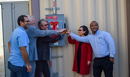 Four people doing a team high-five in front of a fire extinguisher in an office hallway