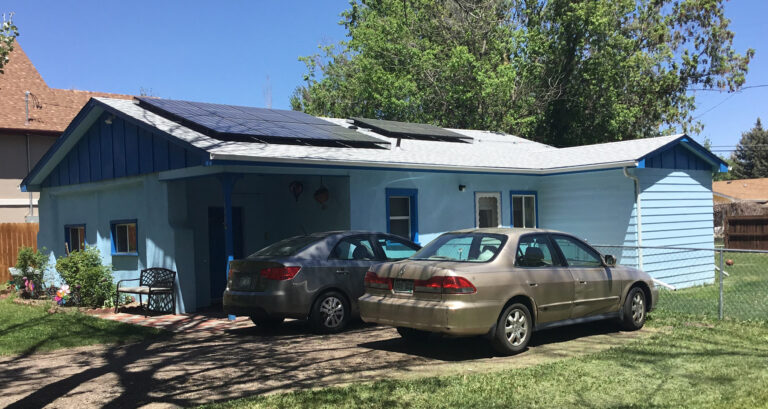 Blue residential house with solar panels on roof and two parked cars in driveway