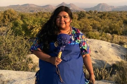Woman in blue dress standing on rocky outcrop with forested hills behind her
