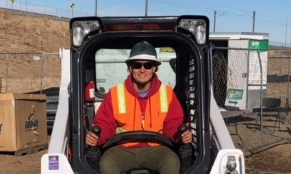 Worker in orange safety vest and hard hat operating compact equipment at job site
