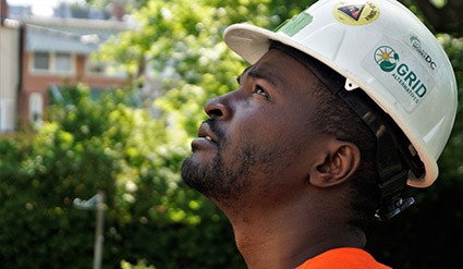 Male worker wearing white hard hat with GRID logo, looking upward outdoors