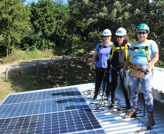 Three people in safety gear stand beside solar panels at El Regadío, Nicaragua installation site