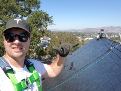 Solar panel installer on rooftop wearing safety gear with valley view in background