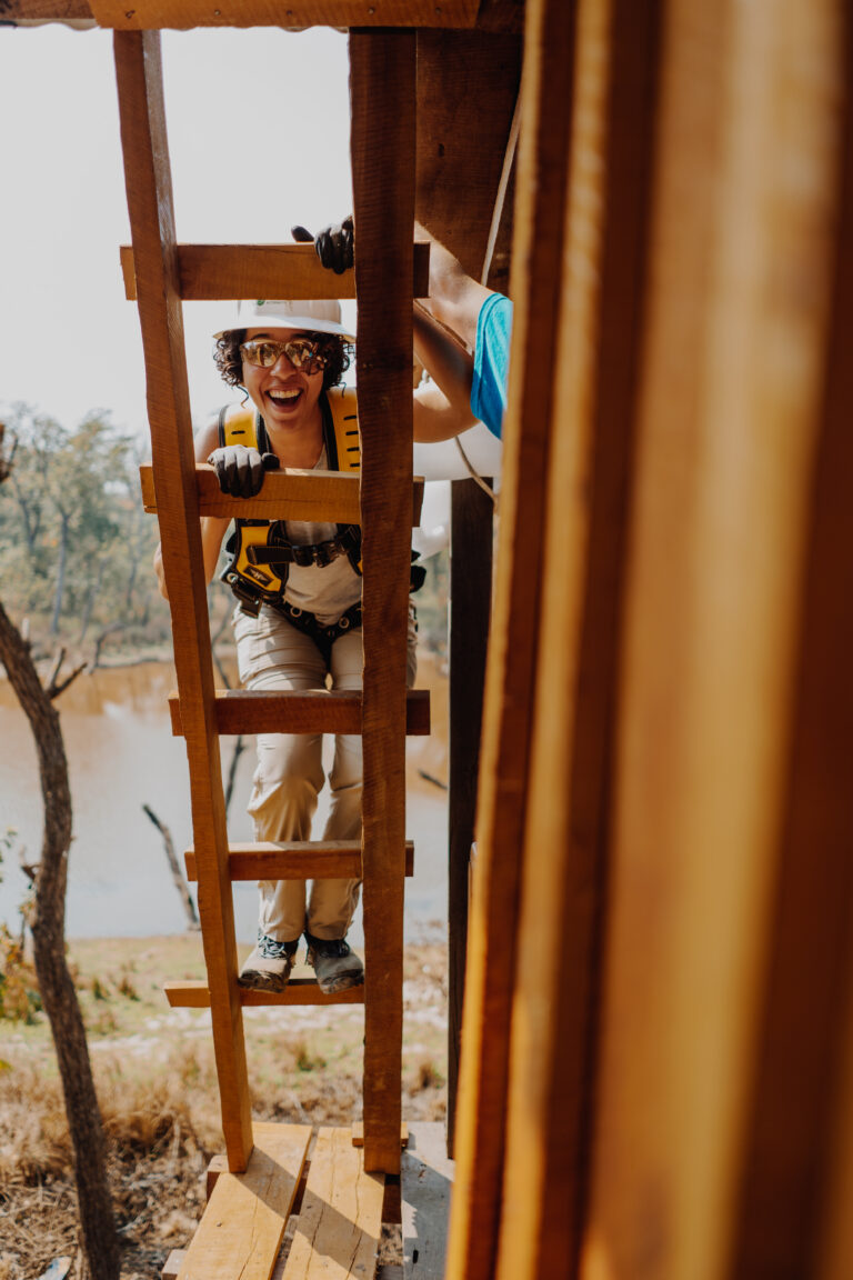 Woman climbing wooden ladder while wearing safety gear and harness