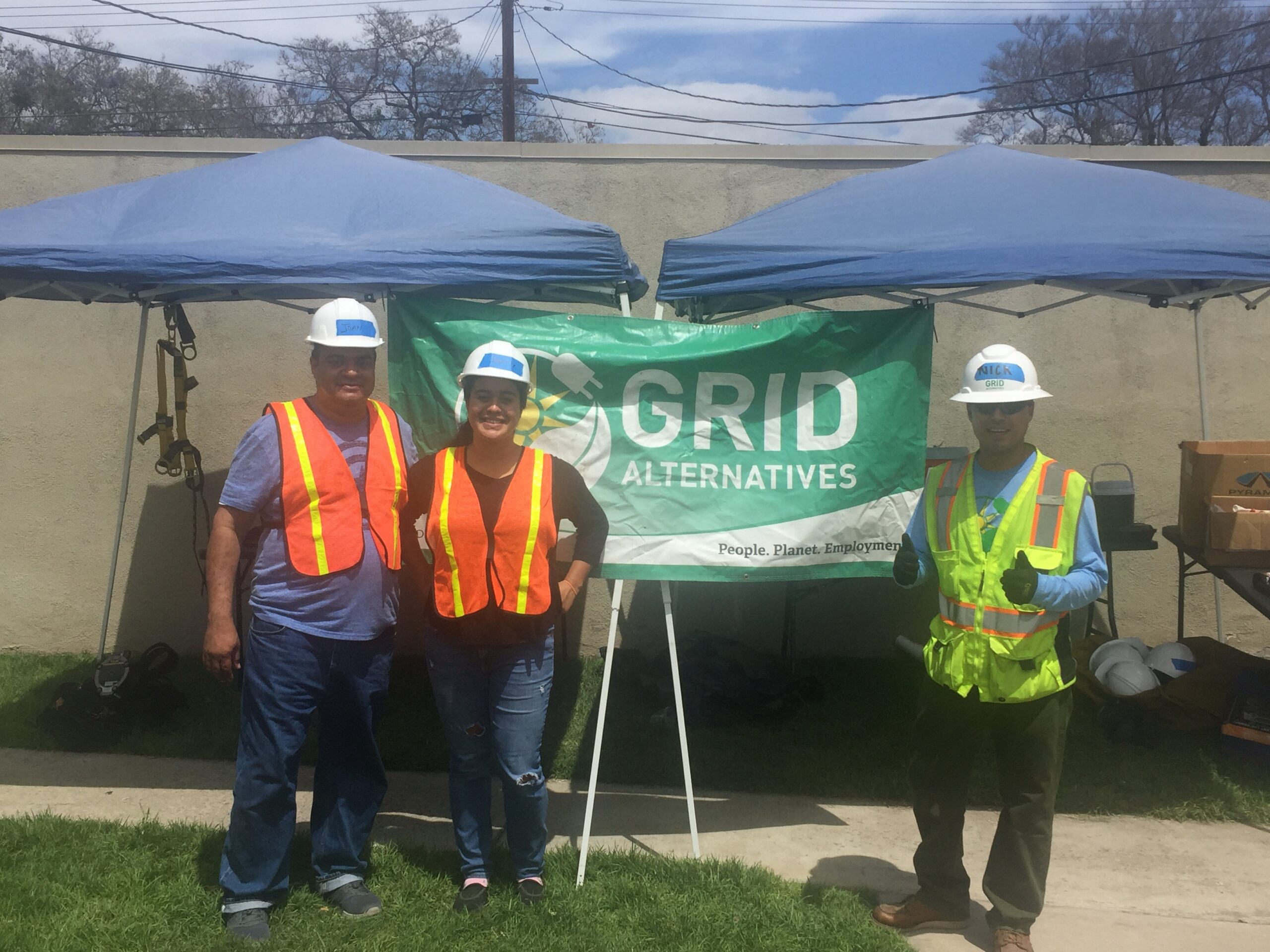 Two family members who are dressed like they are finishing a day as solar trainees stand next to a construction worker in GRID Alternatives gear