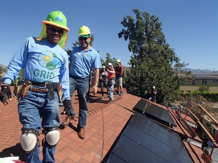 GRID staff in hard hats smile next to a newly installed rooftop solar array.